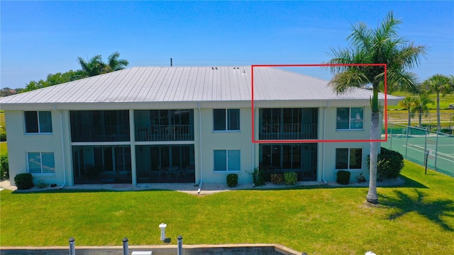 rear view of property with fence, metal roof, a lawn, and stucco siding