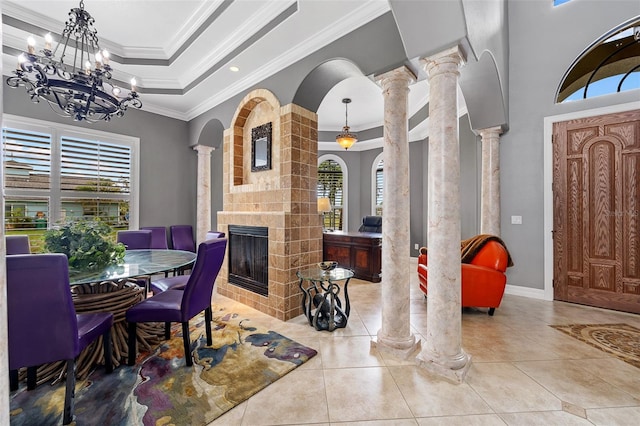 dining area featuring a tiled fireplace, ornate columns, a tray ceiling, a notable chandelier, and tile floors