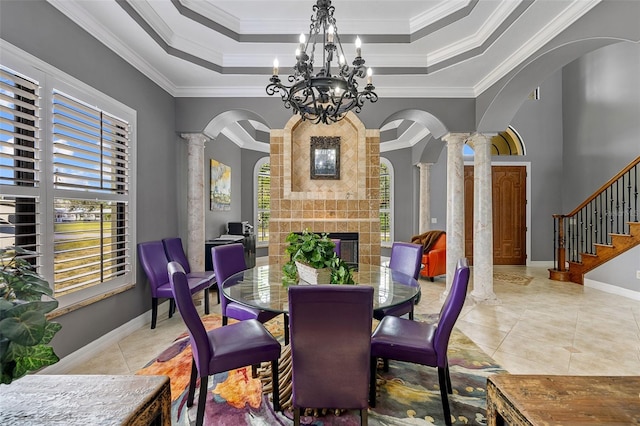 tiled dining room with a notable chandelier, ornate columns, a fireplace, and a raised ceiling