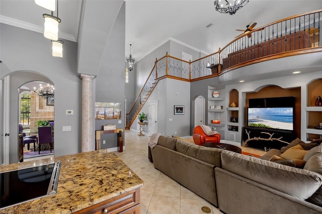 tiled living room featuring ceiling fan with notable chandelier, crown molding, built in features, a towering ceiling, and ornate columns