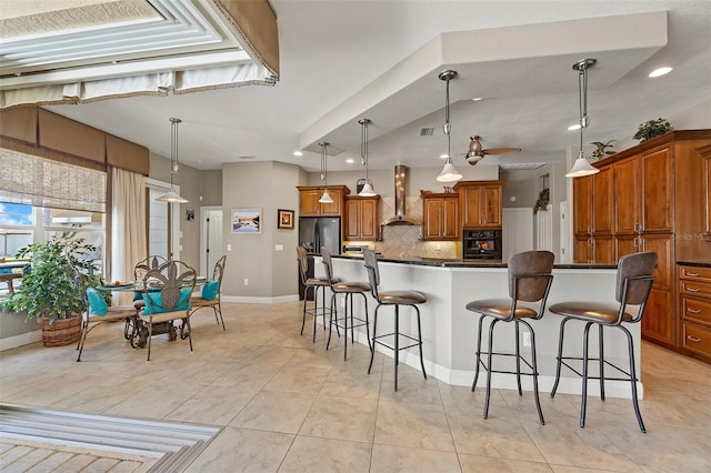 kitchen featuring decorative light fixtures, wall chimney range hood, tasteful backsplash, and black appliances