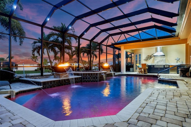 pool at dusk with a patio area, a lanai, area for grilling, and pool water feature