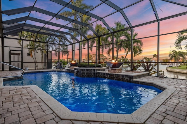 pool at dusk featuring a hot tub, a patio area, a lanai, and pool water feature