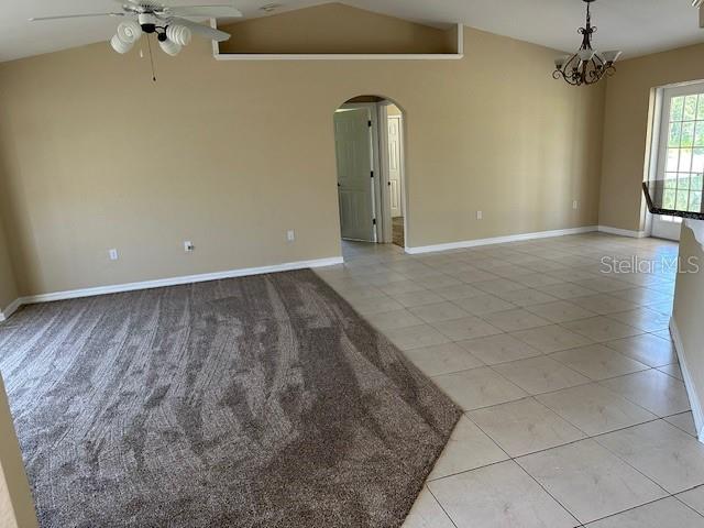 tiled spare room with vaulted ceiling and ceiling fan with notable chandelier