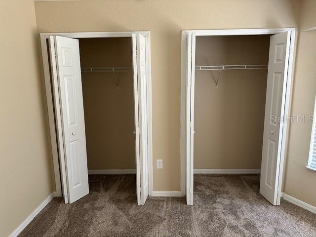 unfurnished bedroom with two closets and dark colored carpet