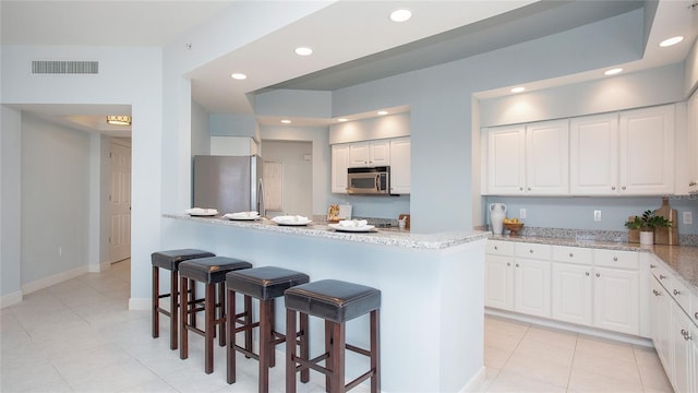 kitchen with appliances with stainless steel finishes, light tile floors, white cabinetry, a breakfast bar area, and light stone countertops