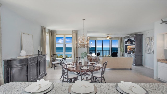 tiled dining area with ceiling fan with notable chandelier, expansive windows, and a water view