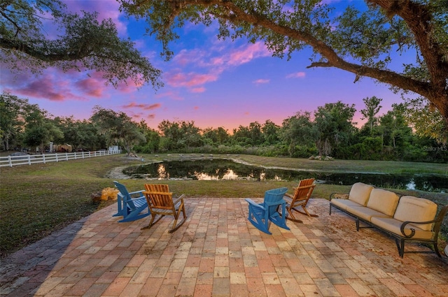 patio terrace at dusk featuring an outdoor living space, a water view, and a lawn