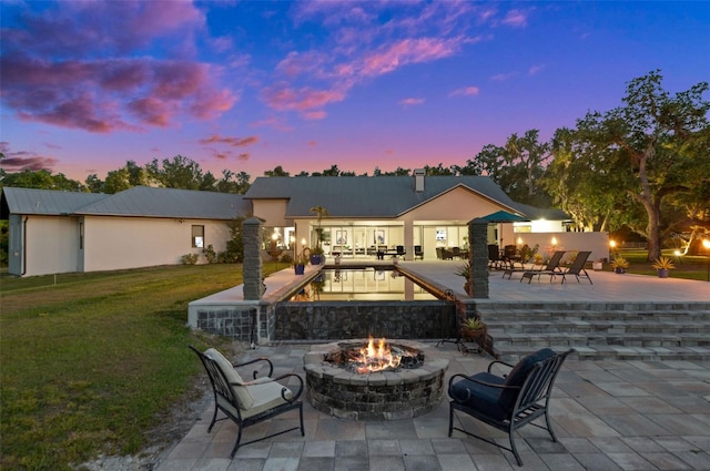 back house at dusk featuring a lawn, an outdoor fire pit, and a patio