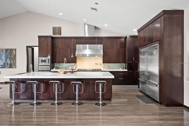 kitchen with built in appliances, hardwood / wood-style floors, dark brown cabinets, and exhaust hood