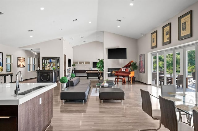 interior space featuring high vaulted ceiling, sink, light hardwood / wood-style flooring, and an island with sink