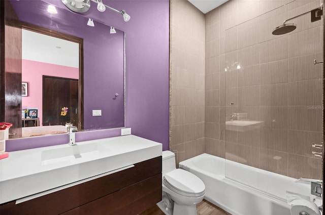 full bathroom with wood-type flooring, tiled shower / bath, vanity, and toilet