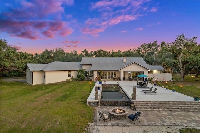 back house at dusk featuring a patio, an outdoor fire pit, and a yard