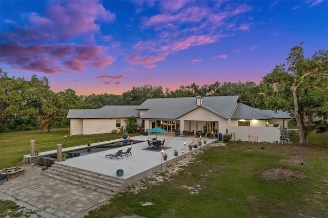 back house at dusk featuring a patio area, a fire pit, and a lawn