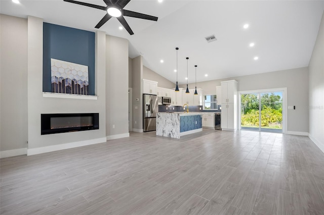 unfurnished living room featuring light hardwood / wood-style floors, a large fireplace, sink, high vaulted ceiling, and ceiling fan