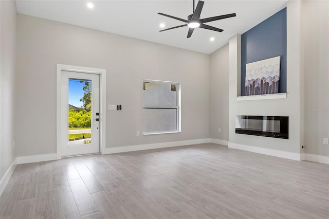 unfurnished living room with a large fireplace, light wood-type flooring, and ceiling fan