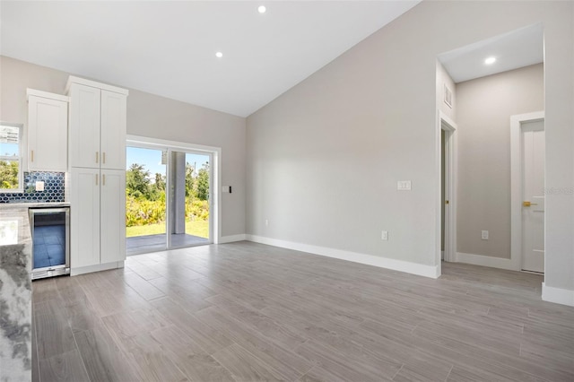 unfurnished living room featuring indoor bar, light hardwood / wood-style floors, wine cooler, and lofted ceiling