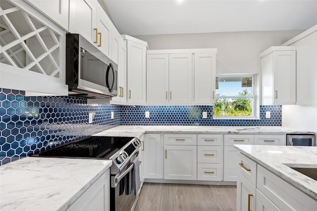 kitchen with light stone countertops, decorative backsplash, white cabinets, light wood-type flooring, and stainless steel appliances