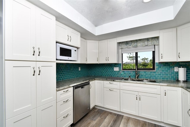 kitchen with white cabinets, white microwave, light wood-type flooring, tasteful backsplash, and stainless steel dishwasher