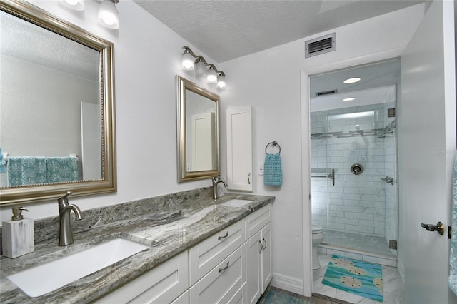 bathroom with a shower with door, dual bowl vanity, toilet, a textured ceiling, and tile floors