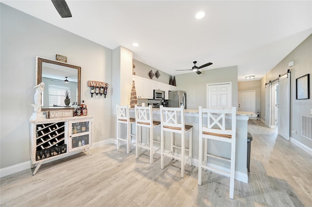 kitchen featuring light hardwood / wood-style flooring, white cabinetry, a barn door, appliances with stainless steel finishes, and ceiling fan