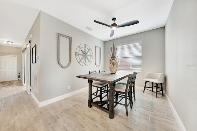 dining area with light hardwood / wood-style flooring, ceiling fan, and a barn door