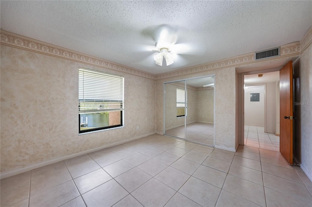 unfurnished bedroom featuring a textured ceiling, ceiling fan, a closet, and light tile floors