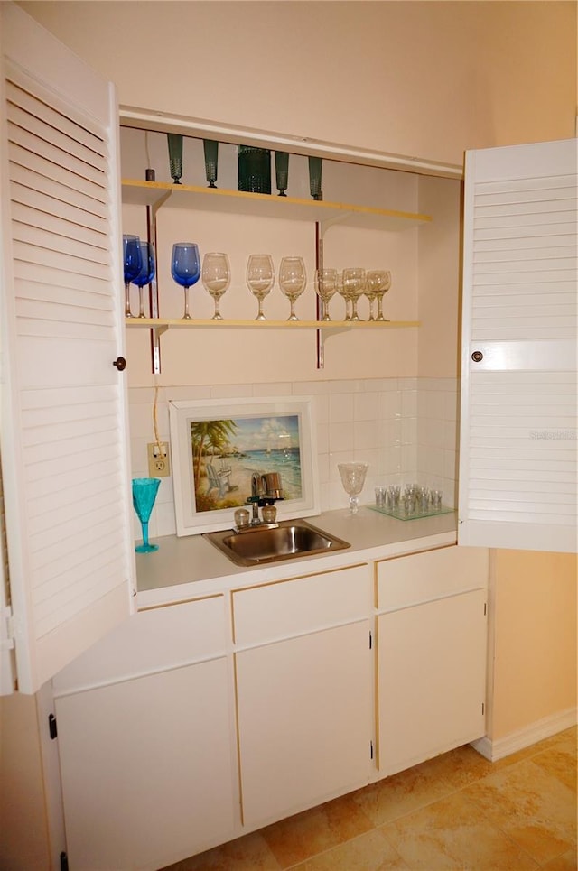 bar featuring sink, tasteful backsplash, light tile floors, and white cabinetry