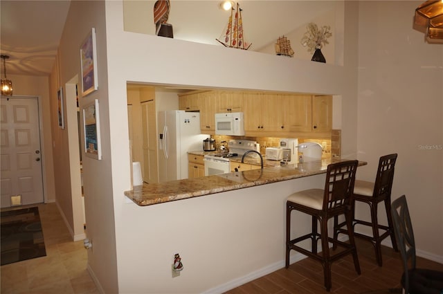 kitchen featuring tile flooring, light stone counters, light brown cabinetry, white appliances, and kitchen peninsula