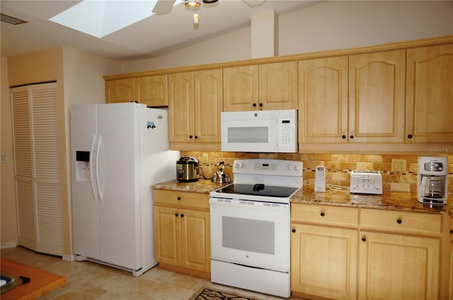 kitchen with white appliances, light stone countertops, vaulted ceiling with skylight, backsplash, and ceiling fan