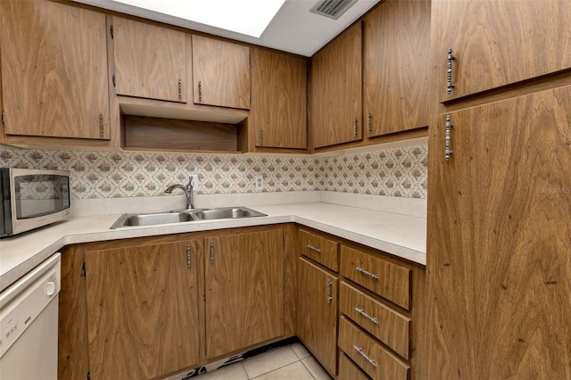 kitchen featuring a skylight, dishwasher, light tile patterned flooring, and sink