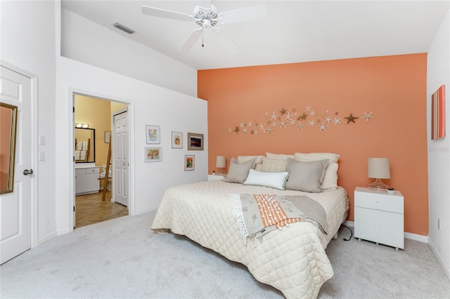 bedroom with ceiling fan, light colored carpet, and ensuite bath