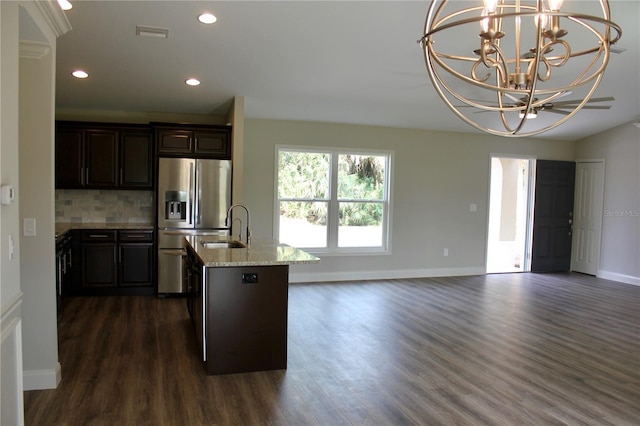 kitchen featuring light stone counters, backsplash, dark wood-type flooring, a center island with sink, and an inviting chandelier