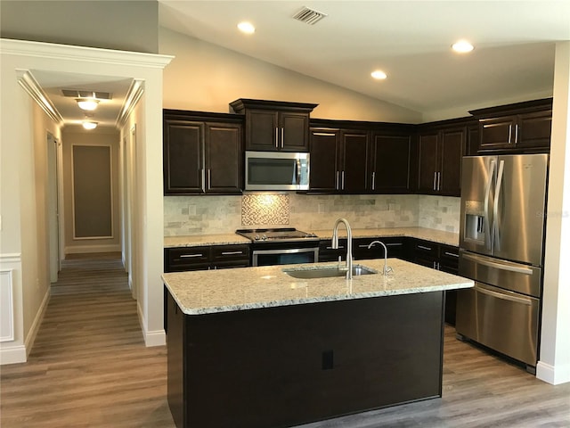 kitchen featuring appliances with stainless steel finishes, backsplash, light hardwood / wood-style floors, lofted ceiling, and an island with sink