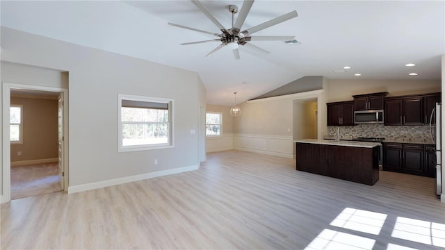 kitchen with vaulted ceiling, appliances with stainless steel finishes, a center island with sink, and light wood-type flooring