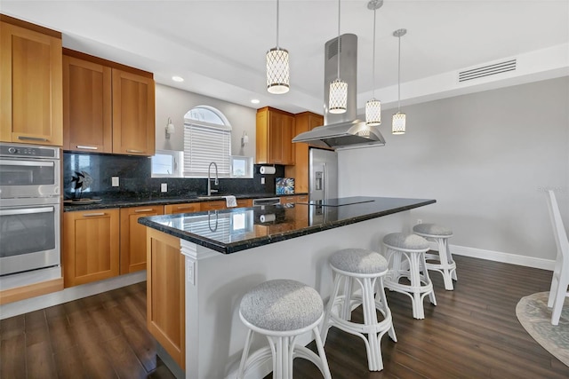 kitchen featuring decorative light fixtures, backsplash, island exhaust hood, dark wood-type flooring, and appliances with stainless steel finishes