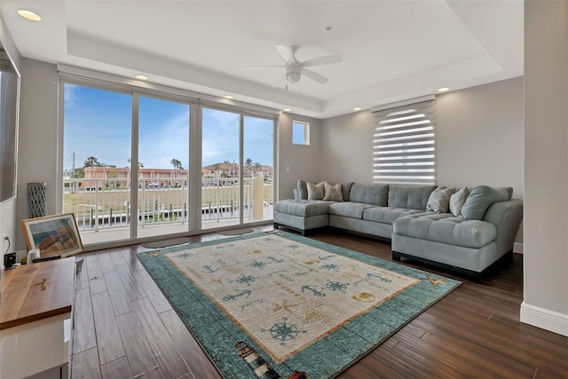 living room featuring dark hardwood / wood-style floors, ceiling fan, and a raised ceiling