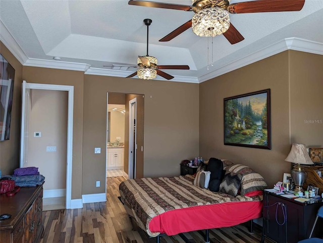 bedroom featuring wood-type flooring, ceiling fan, a tray ceiling, ensuite bath, and crown molding