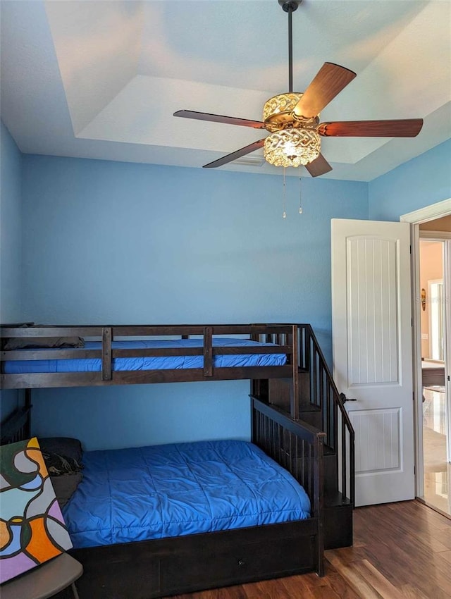 bedroom with wood-type flooring, ceiling fan, and a tray ceiling