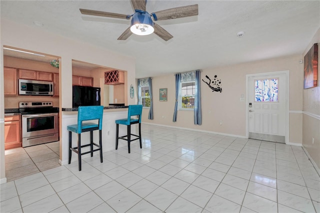 kitchen with appliances with stainless steel finishes, a breakfast bar area, ceiling fan, and light tile floors