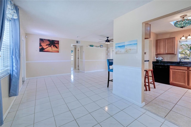 interior space featuring black dishwasher, ceiling fan, light tile floors, and dark stone counters