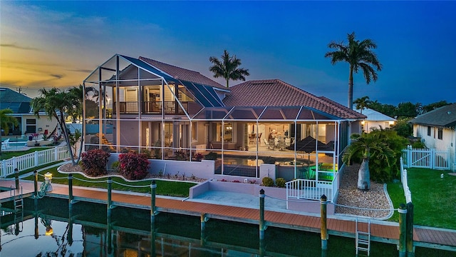 back house at dusk with glass enclosure and a lawn