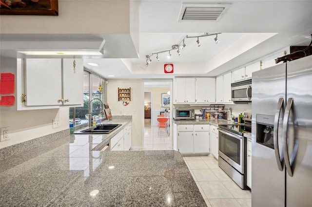 kitchen with appliances with stainless steel finishes, white cabinets, track lighting, and a tray ceiling