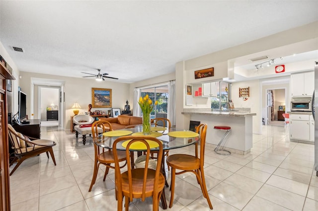 tiled dining space featuring ceiling fan, rail lighting, and a textured ceiling