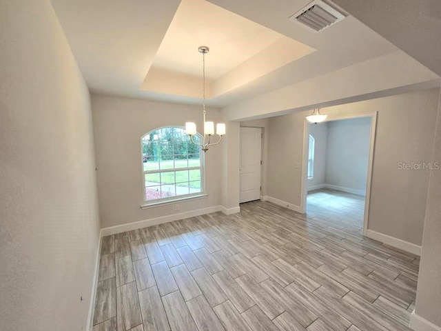 unfurnished dining area featuring a raised ceiling, light wood-type flooring, and a notable chandelier