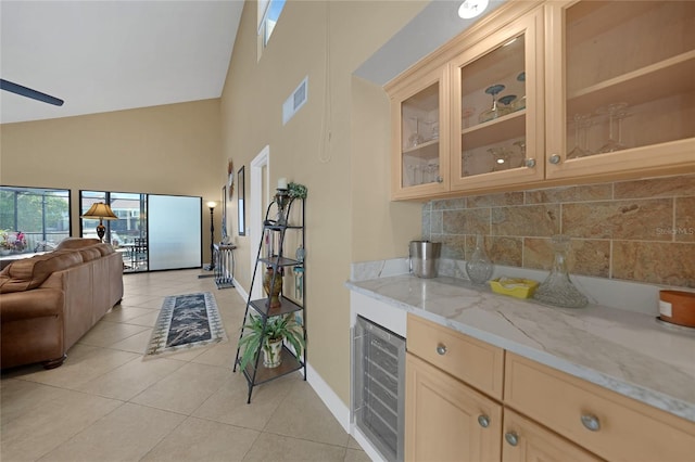 kitchen featuring light stone counters, light tile floors, wine cooler, high vaulted ceiling, and backsplash