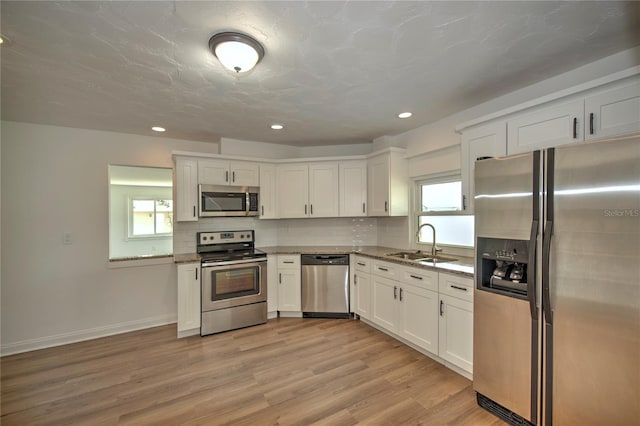 kitchen with appliances with stainless steel finishes, light hardwood / wood-style flooring, white cabinetry, and sink