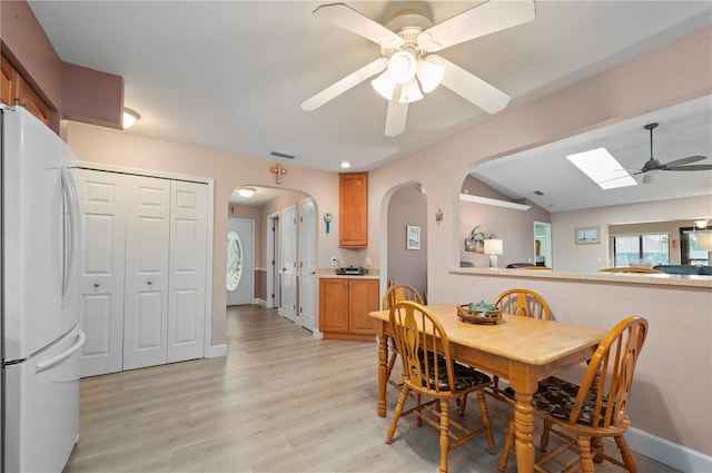 dining space featuring ceiling fan, lofted ceiling with skylight, and light hardwood / wood-style flooring