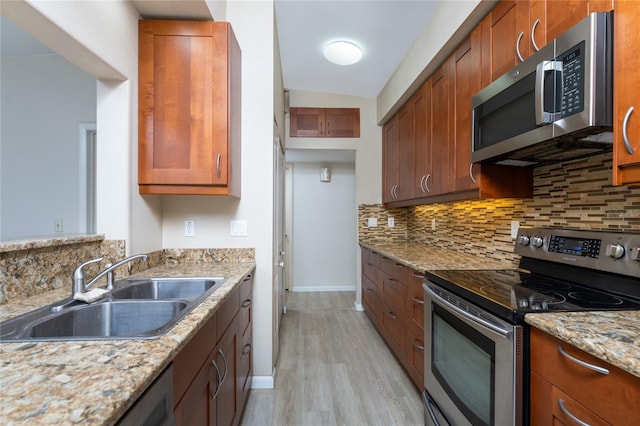 kitchen with light stone counters, stainless steel appliances, sink, and light wood-type flooring