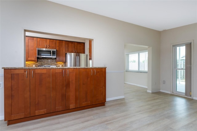 kitchen with light stone counters, stainless steel appliances, decorative backsplash, and light wood-type flooring